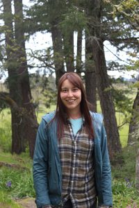 Julia standing and smiling with tall trees in the background