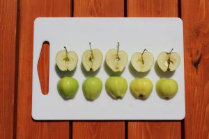 A row of apples sits cut in half on a cutting board in order of ripeness, ranging from a light green to a light yellow