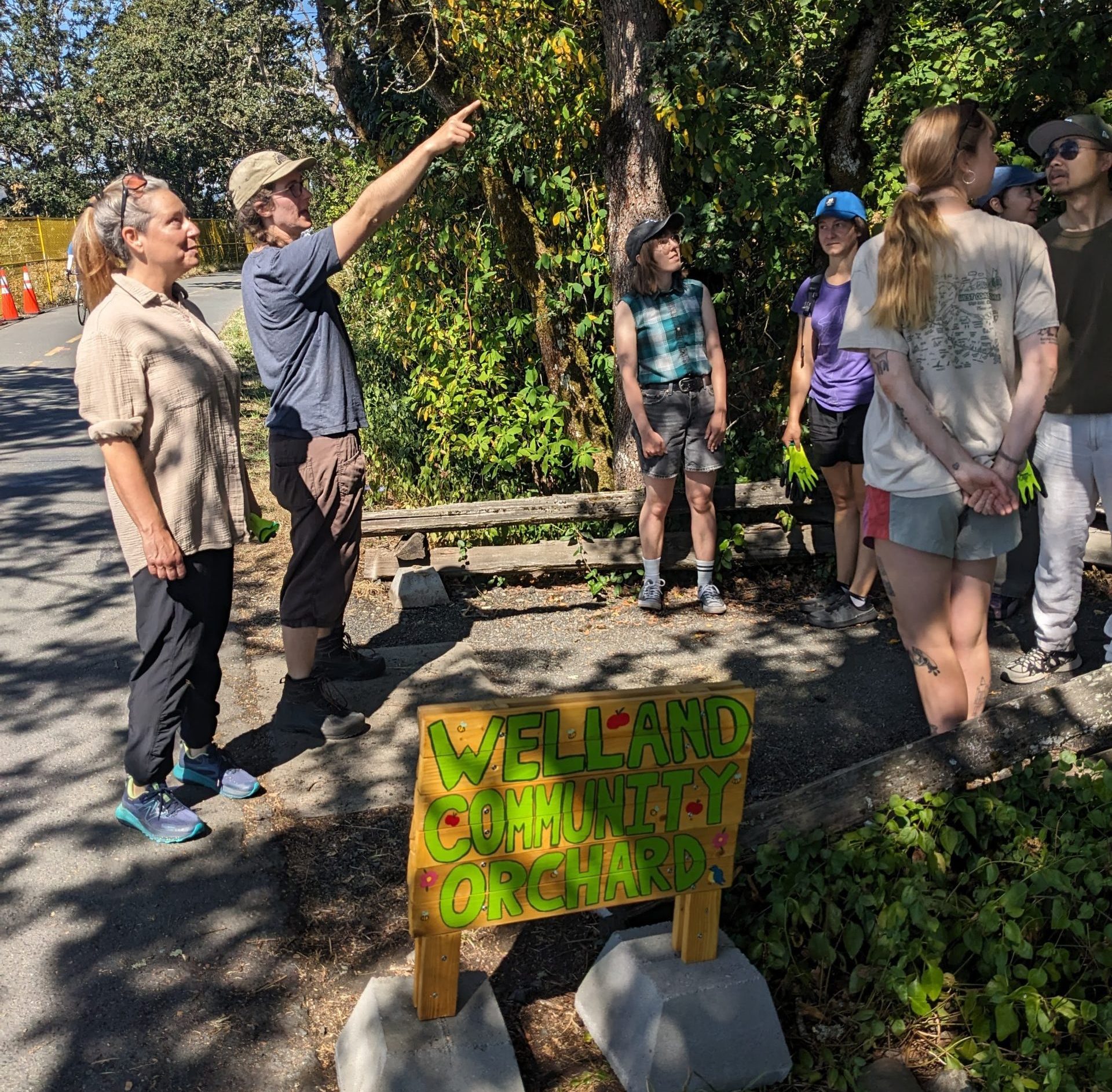 The Welland Orchard Manager showing visitors around the orchard, with a Welland Community Orchard sign in view.